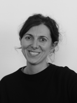 Schwarzweißes Portrait von Anna Martinez. Weibliche, lächelnde Person mit dunklen Haaren im Zopf.