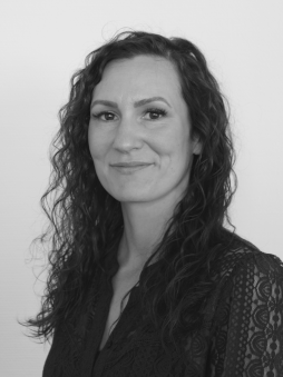 Schwarzweißes Portrait von Caroline Kluge. Weibliche Person mit lockigen Haaren, die zugewandt guckt.